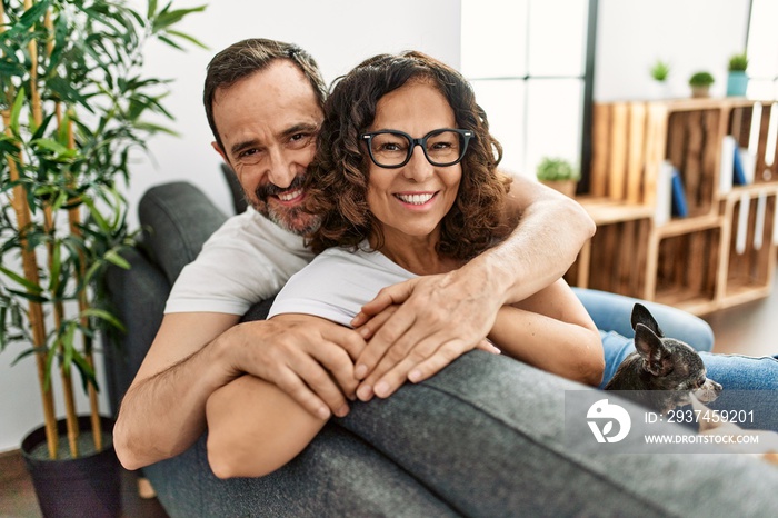 Middle age hispanic couple smiling happy sitting on the sofa with dogs at home.