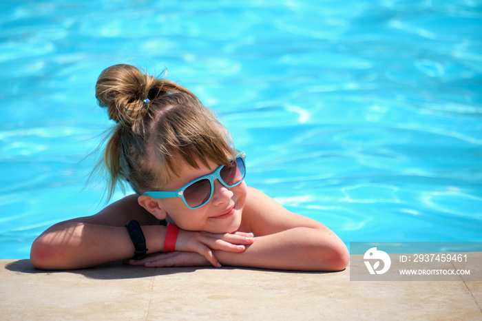 阳光明媚的夏日，年轻快乐的小女孩在游泳池边休息，池水清澈湛蓝。Tro