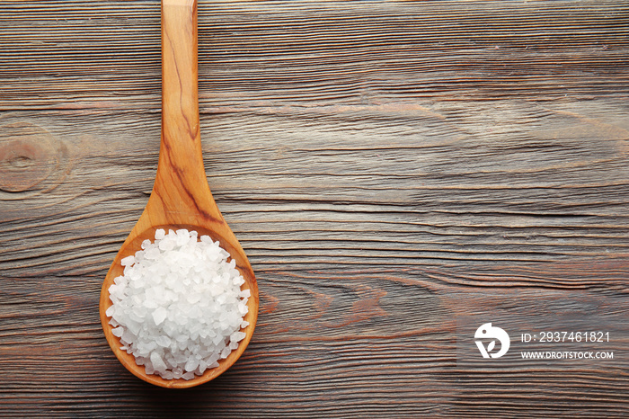 Spoon with sea salt on wooden background