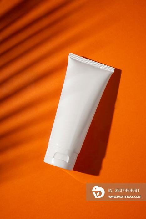 Plastic white bottle for cream or lotion on a orange background. Skincare cosmetic with beautiful pa