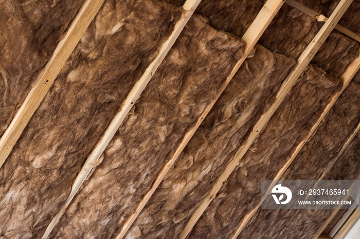 Brown glass wool in a wooden frame on a inclined wall near the wooden ceiling in a private house. Wa