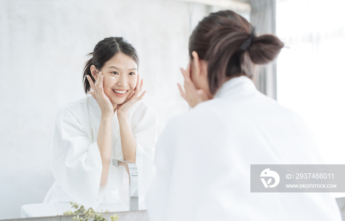 Female Skin Care. Young asian woman touching her face and looking to mirror in bathroom