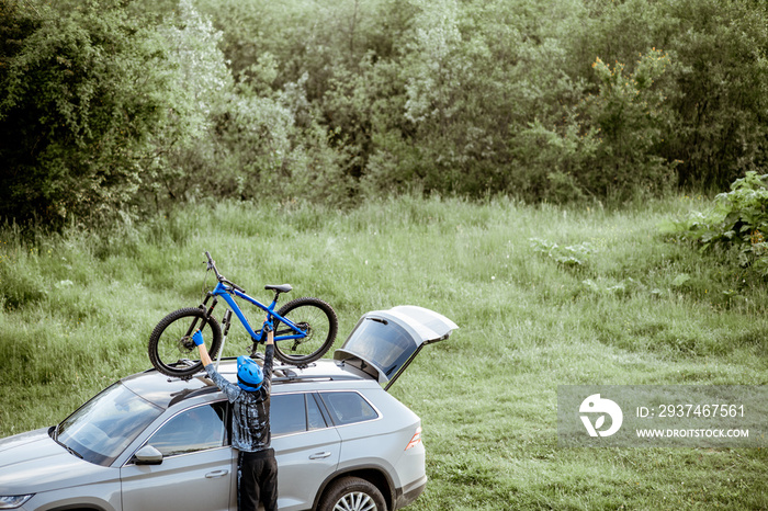 Professional cyclist taking bicycle from the car roof trunk while standing on the green meadow in th