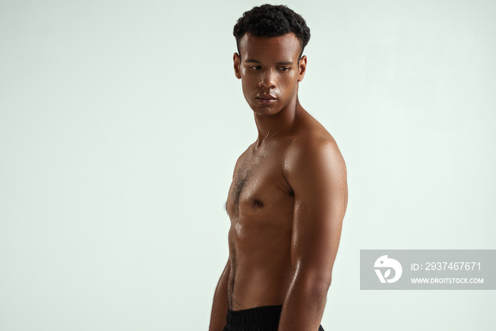 Side view of young shirtless muscular african man looking away while standing against grey backgroun