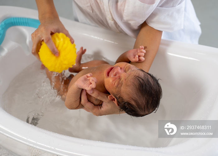 White shirt mother use yellow sponge to bath little newborn baby in white bathtub