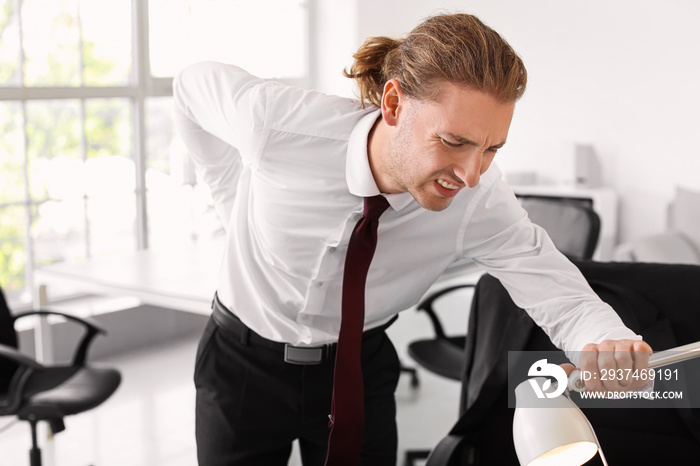 Young man suffering from back pain in office