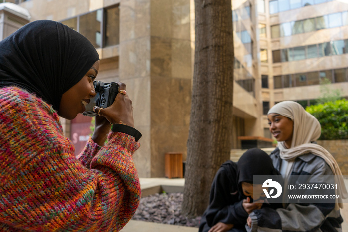 Young woman photographing friends wearing hijabs in city