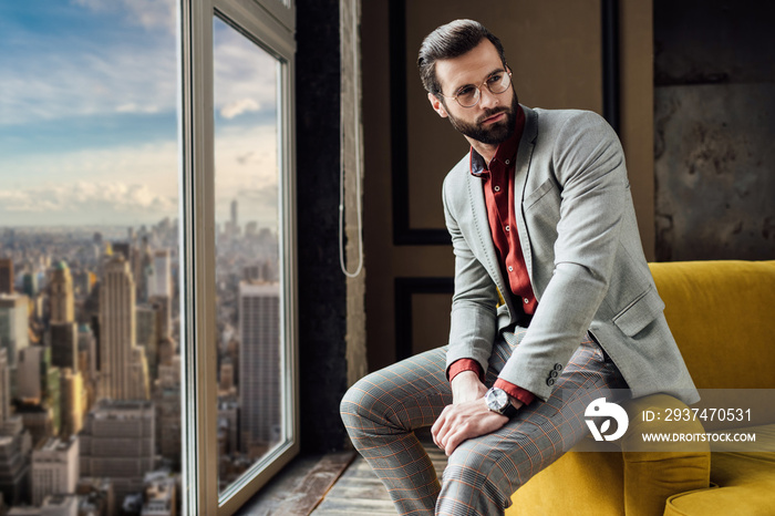 stylish man in suit posing at window with city view