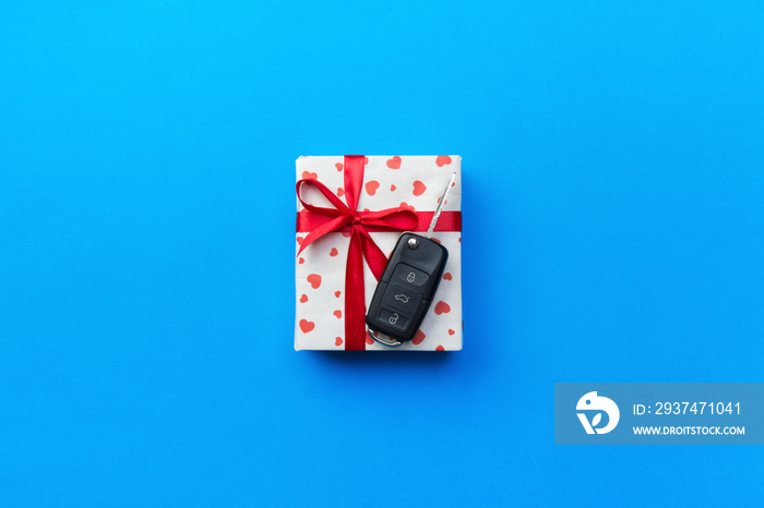 Give gift car key concept top view. Present box with red ribbon bow, heart and car key on blue color