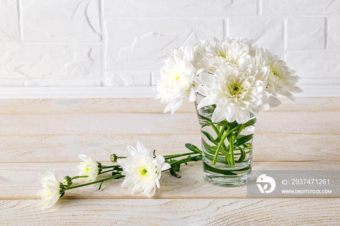 Small modest bouquet of white lush chrysanthemums in a glass vase on a white wooden table. To give f