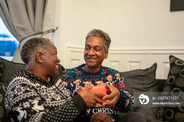 Senior couple sitting on sofa holding Christmas gifts