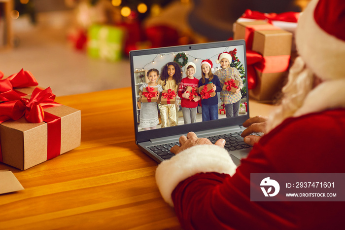 Santa Claus having video call with group of diverse kids using laptop computer in his workshop