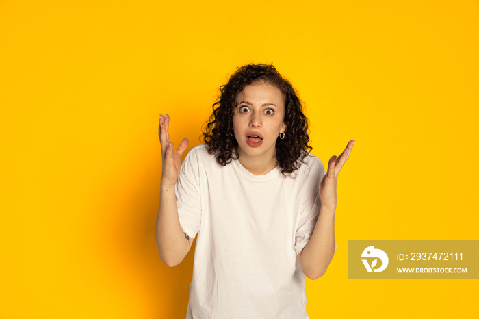 One surprised young beautiful girl in white t-shirt wondering isolated on yellow background. Concept