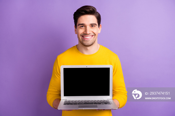 Photo of young happy positive smiling man show laptop display advertising product isolated on violet