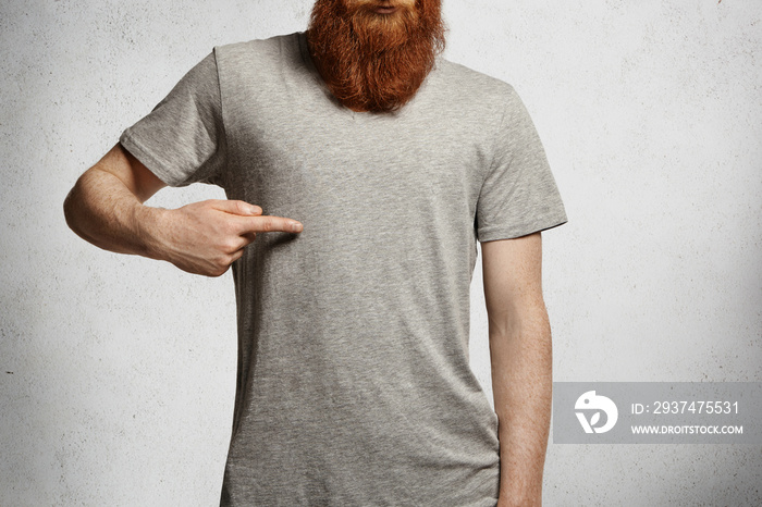 Design and advertising concept. Cropped shot of stylish young man with hipster red beard pointing in