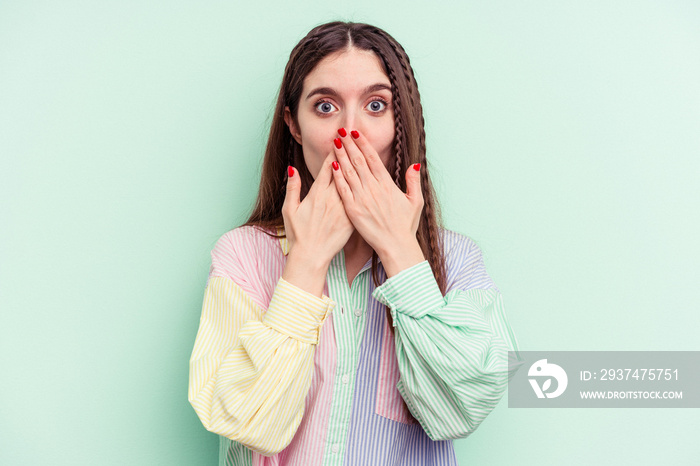 Young caucasian woman isolated on green background shocked covering mouth with hands.