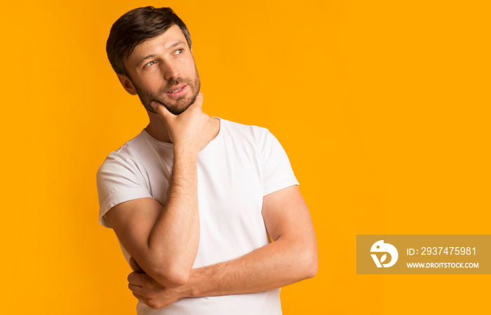 Pensive middle-aged guy standing touching chin thinking over yellow background