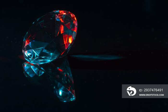 Closeup of a diamond on a black mirror surface with red and blue highlights