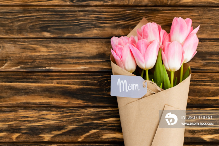 母亲节当天，木质表面用纸包裹的粉红色郁金香上印有母亲字样的标签俯视图