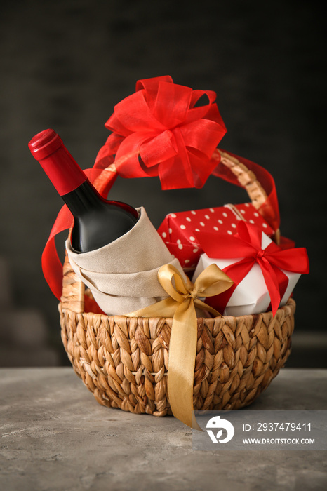 Wine bottle with gift boxes in wicker basket on dark background