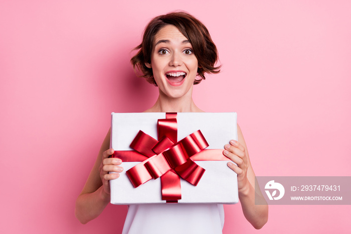 Portrait of attractive cheerful lucky brown-haired girl holding in hands gift having fun isolated ov