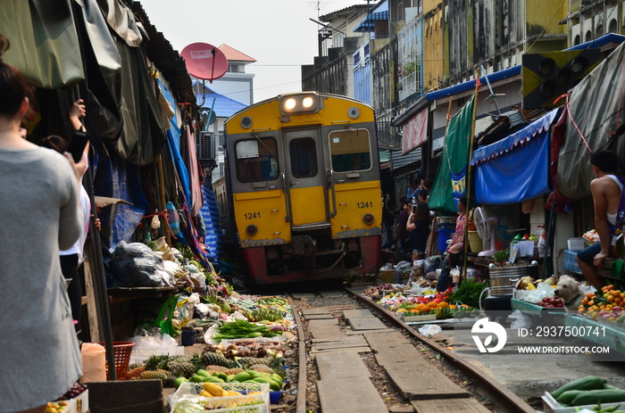 タイの首都のバンコク　メークロン鉄道市場　線路沿いの屋台と電車が通過する光景