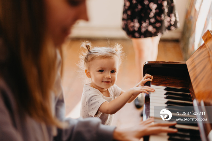 Cute little happy child girl playing piano in a light room. Selective focus, noise effect