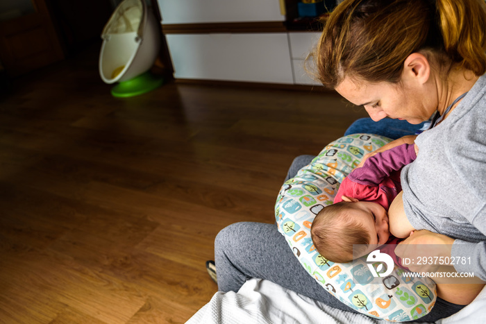 Profile portrait of a young woman breastfeeding a child using a special breastfeeding pillow for new