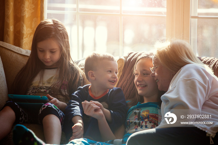 Grandmother with grandchildren (2-3, 10-11) sitting on sofa