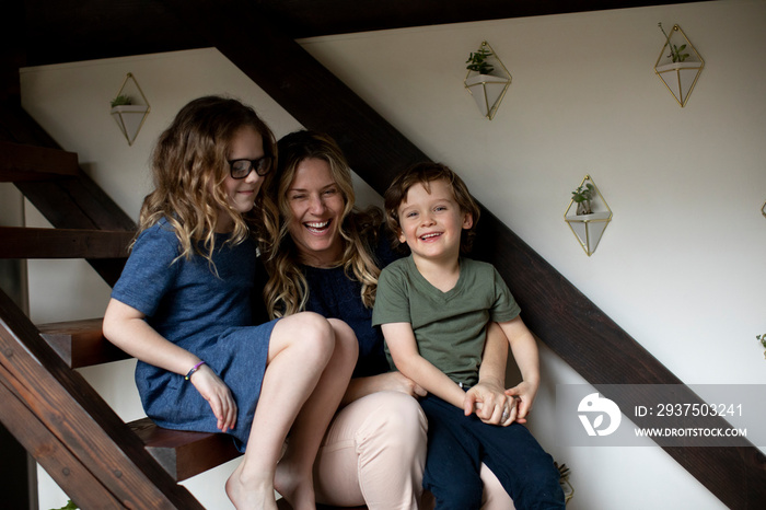 Portrait of happy mother with cute children sitting on steps against wall at home