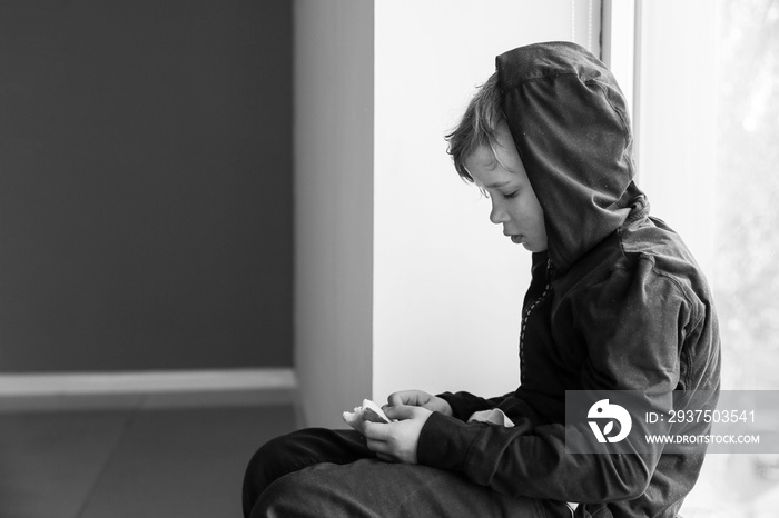 Homeless little boy with bread sitting on window sill indoors