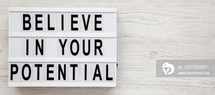 Believe in your potential words on a lightbox on a white wooden background, top view. Flat lay, ov