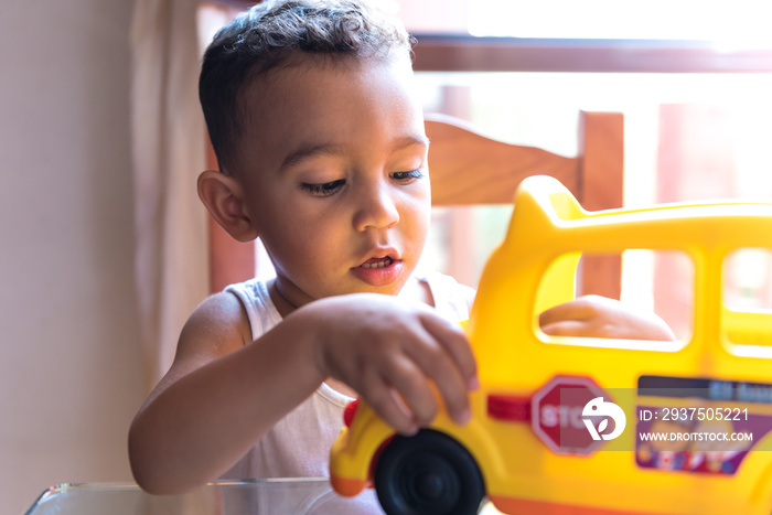 Child boy playing with a school bus toy indoors.