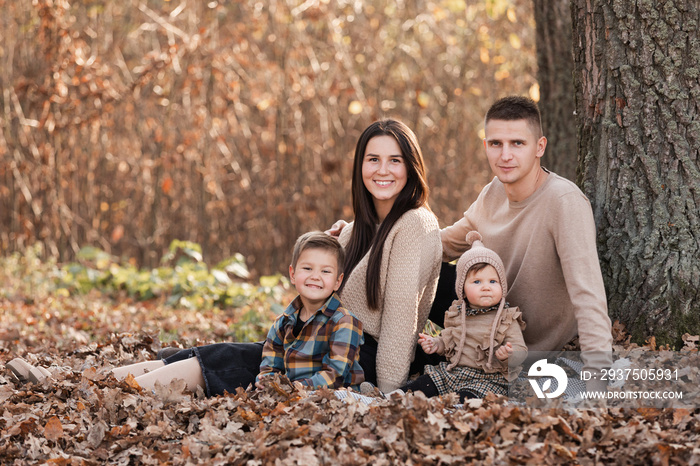 young dad and mom with baby girl relaxing on blanket in autumn park on sunny day. happy family conce