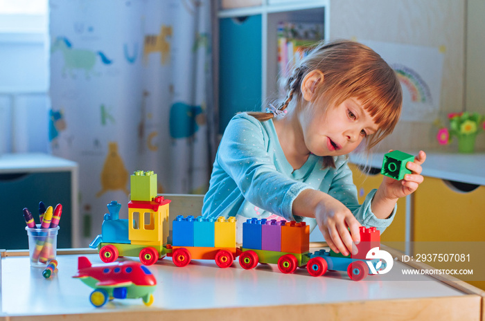 Little girl playing with kids plastic toy train with colorful cubes