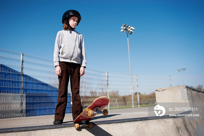 Girl with skateboard looking away while standing at park