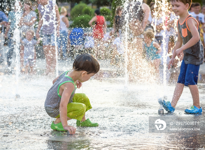 兴奋的男孩在喷泉里的喷水器之间玩得很开心。城市里的夏天