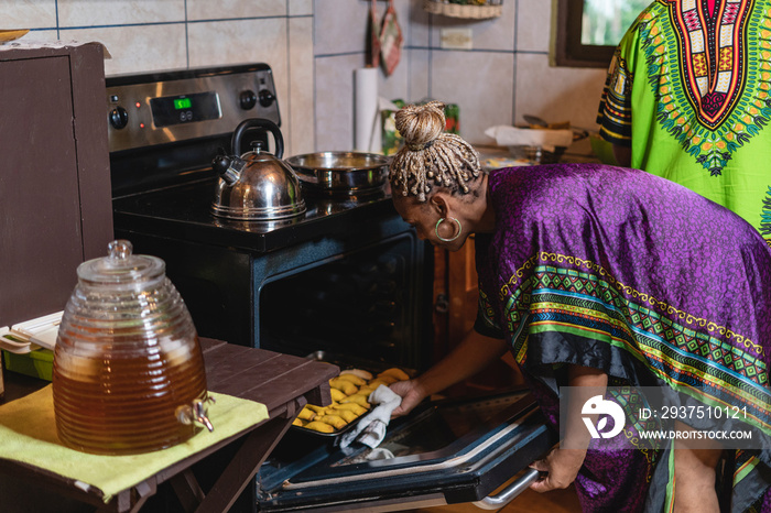 Horizontal de una mujer afrocaribeña en el interior de su cocina sacando del horno unos bocadillos c