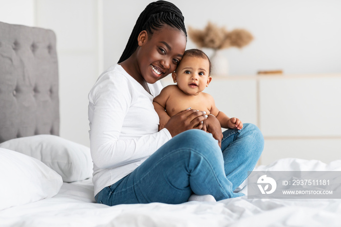 African American mom sitting on bed with her cute baby