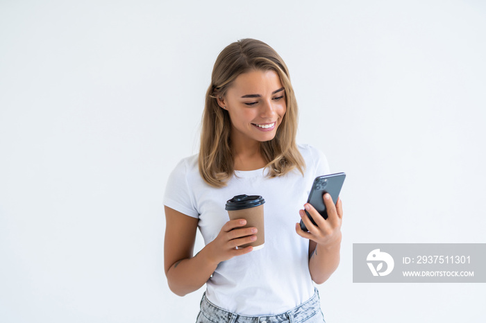 Portrait of a satisfied young woman using mobile phone while holding cup of coffee to go isolated ov