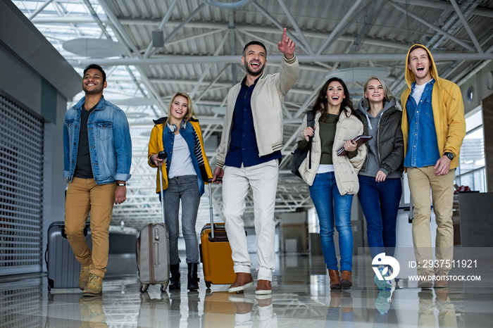 Full length portrait of delighted males and females looking for exit in the airport. They are walkin