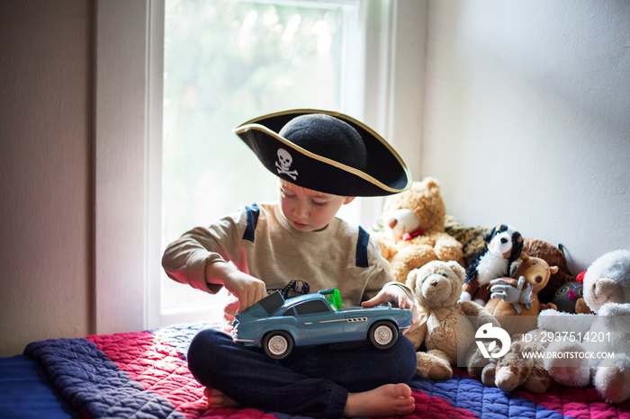 Portrait of boy (2-3) wearing pirate hat sitting on bed playing with toy car