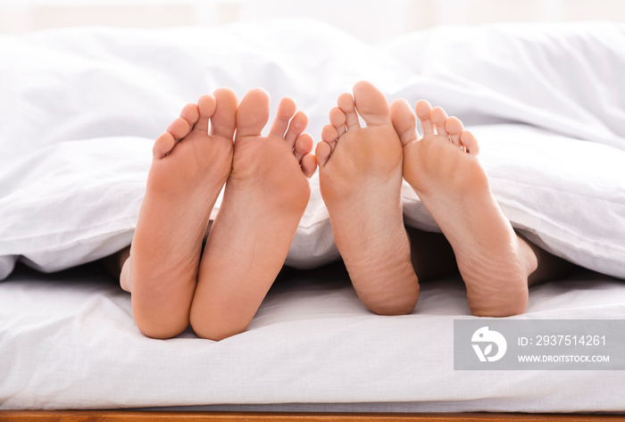 Feet of couple in bed under blanket