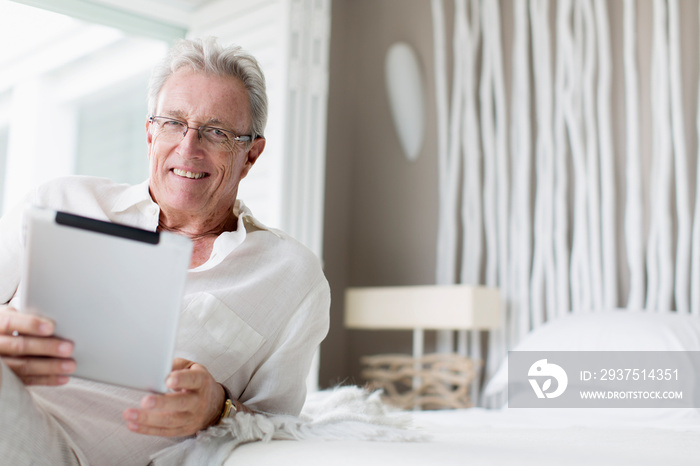 Portrait happy senior man using digital tablet on bed