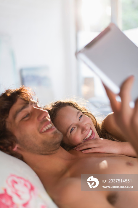 Happy young couple using digital tablet on bed