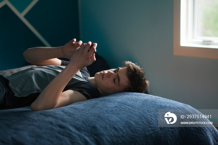 Boy (12-13) using mobile phone on bed