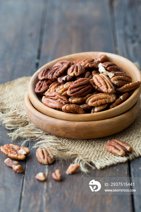 Pecan nuts on a rustic wooden table and pecan nuts in bowl.