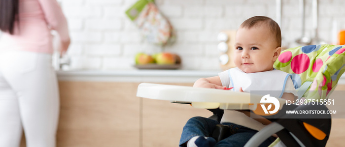 可爱的婴儿坐在厨房高高的儿童椅上