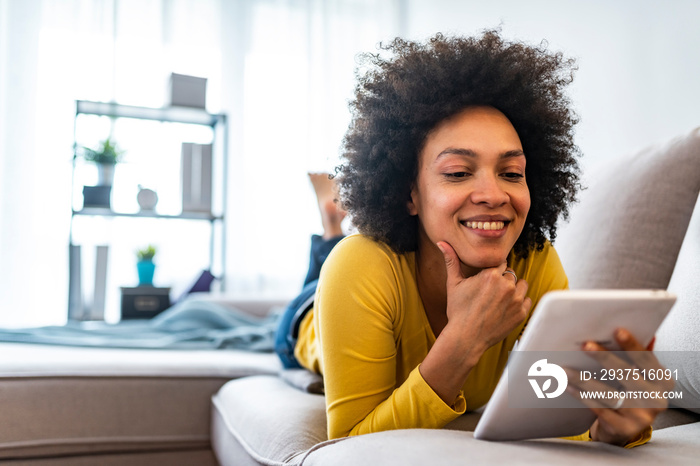 Happy young woman with tablet pc laying on sofa. Young happy woman lie down on bed and playing smart