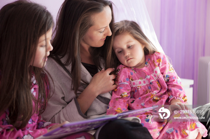 Mom reading to daughters (2-3, 8-9) in bedroom